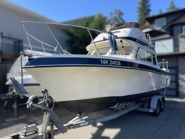 A white and blue Telestar Sedan motorboat on a trailer is parked on a driveway near houses, with trees and a blue sky in the background. The boat’s registration number, 14K 24038, is visible on its side.