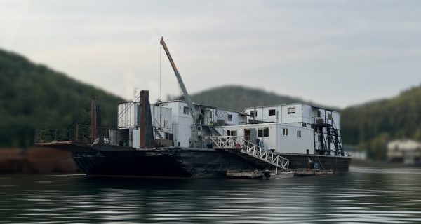 The 21 Person Float Camp features a large barge with white structures and a crane, offering group camping for up to 21 on calm waters, surrounded by forested hills beneath a cloudy sky.