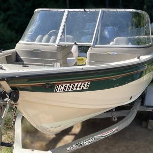 A 2006 Crestliner 1650 Sport Angler (Reg. BC6694455) sits on a trailer, featuring a windshield, seats, and a white body with green and brown stripes; trees and greenery are visible in the background.