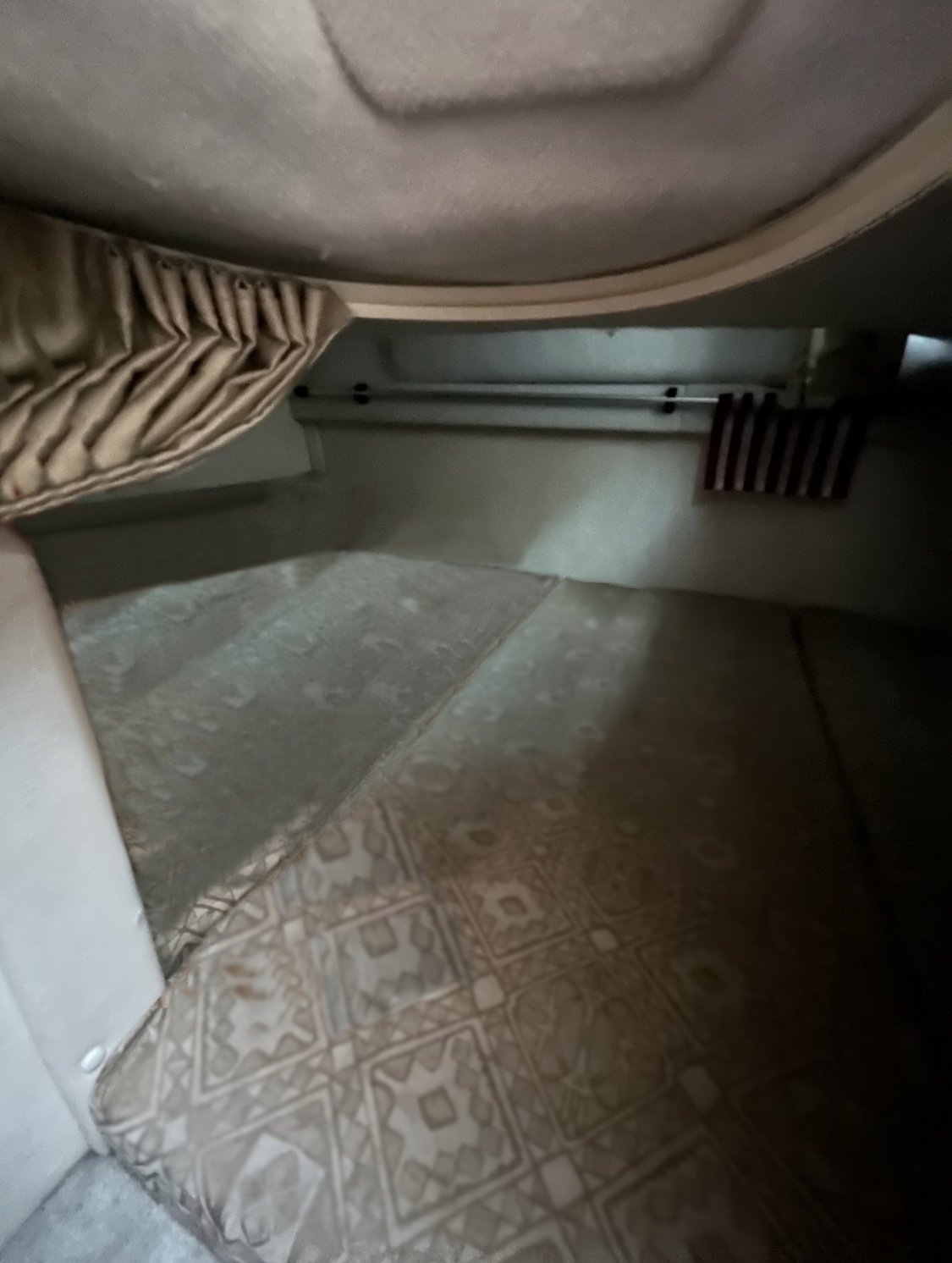 A dimly lit, compact sleeping area with a patterned mattress, beige upholstery, curtain on the left, and small wall rack inside a 2000 / 24FT Monterey 242 boat.