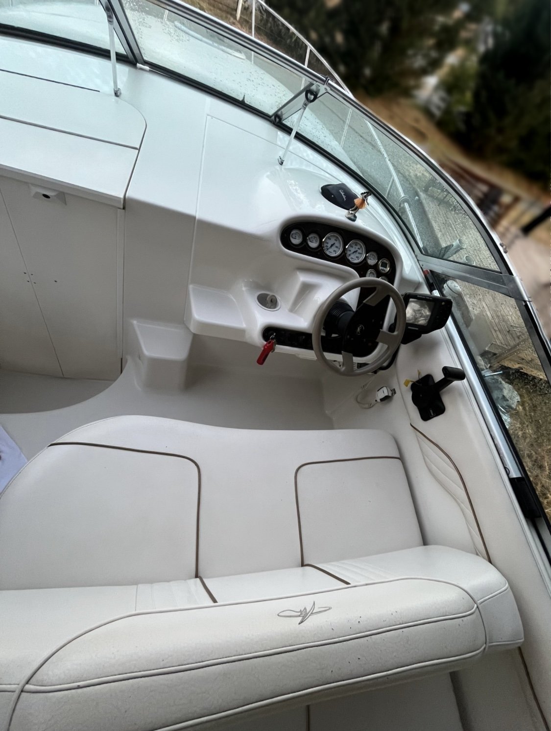 The photo shows the cockpit of a 2000 / 24FT Monterey 242, featuring a steering wheel, gauges, control panels, and cream-colored stitched seats. A windshield wraps around the console of this spacious boat.