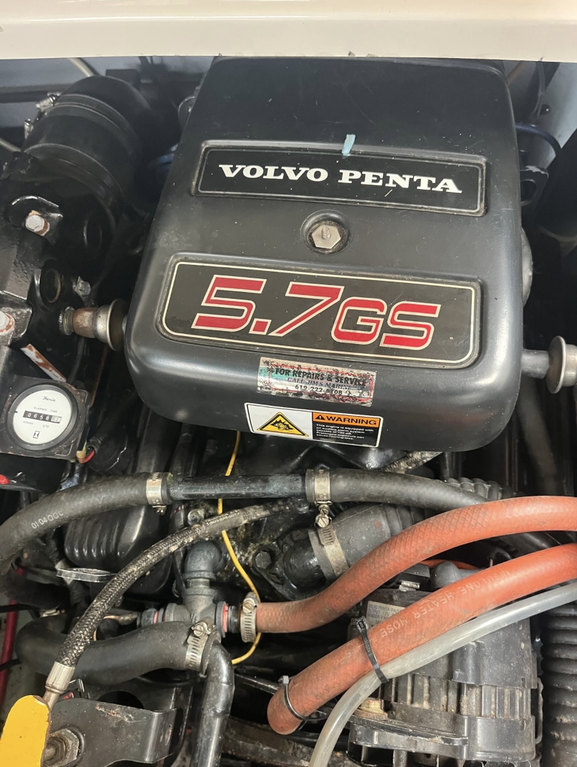 Close-up of a Volvo Penta "5.7 GS" engine in a 2000 / 24FT Monterey 242 boat, displaying hoses, wires, warning labels, and clearly visible engine components and connections.