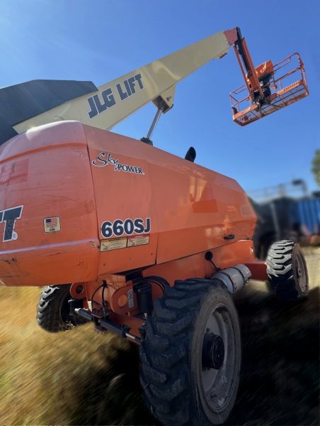 A 2014 JLG 660SJ Man Lift is shown on grassy ground, with its arm extended and basket elevated toward a clear blue sky.