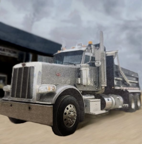 A 2012 Peterbuilt Dump Truck in silver is parked on a sandy surface before a building beneath a cloudy sky.