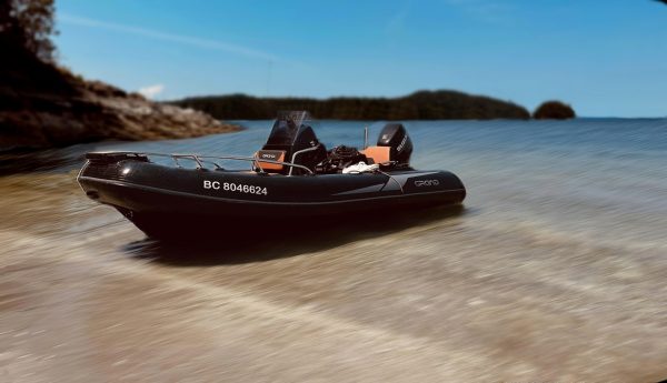 A 2022 / 14FT Golden RIB with "BC 8046624" on its side is beached on sand by calm blue water, surrounded by rocks, trees, and small islands under a clear sky.
