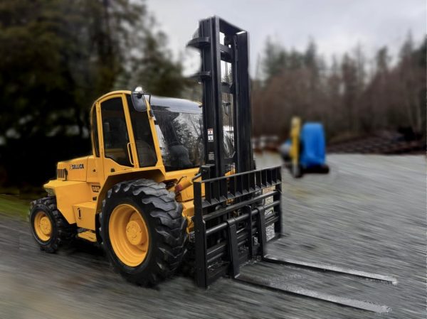 A 2015 Sellick S80 4x4 forklift, 8000lb capacity and yellow in color, with large tires, is parked on gravel near trees and some blurred background objects on a cloudy day.