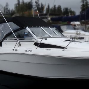 A 2004 / 24FT Campion 682i Sport Cabin motorboat with a black canopy is docked in a marina among other boats, with trees and cloudy skies in the background.