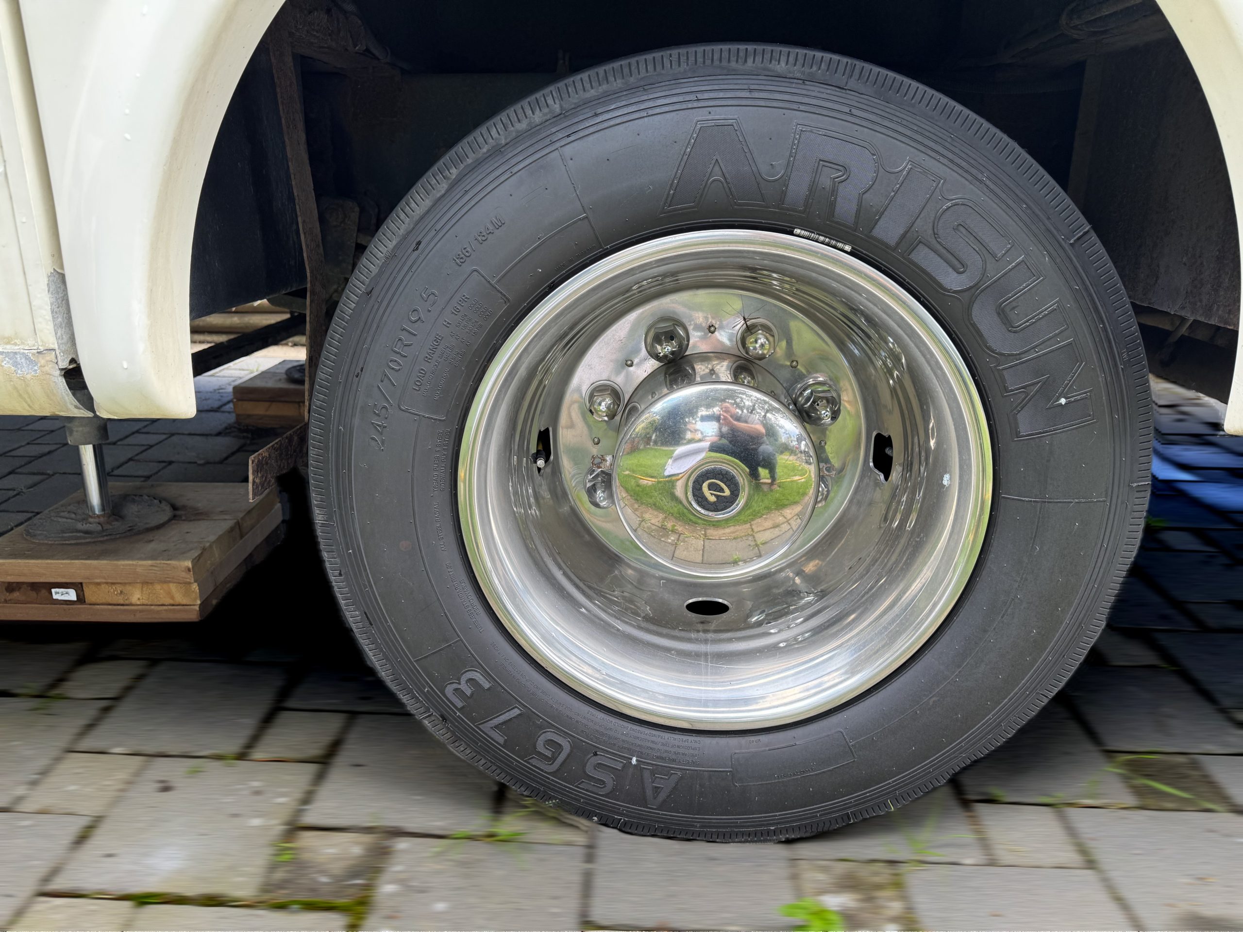 Close-up of a shiny chrome wheel with an Arisun A/S 673 tire on a 2007-10 Dumont Challenger, parked on stone pavers. The photographer's reflection appears in the hubcap.