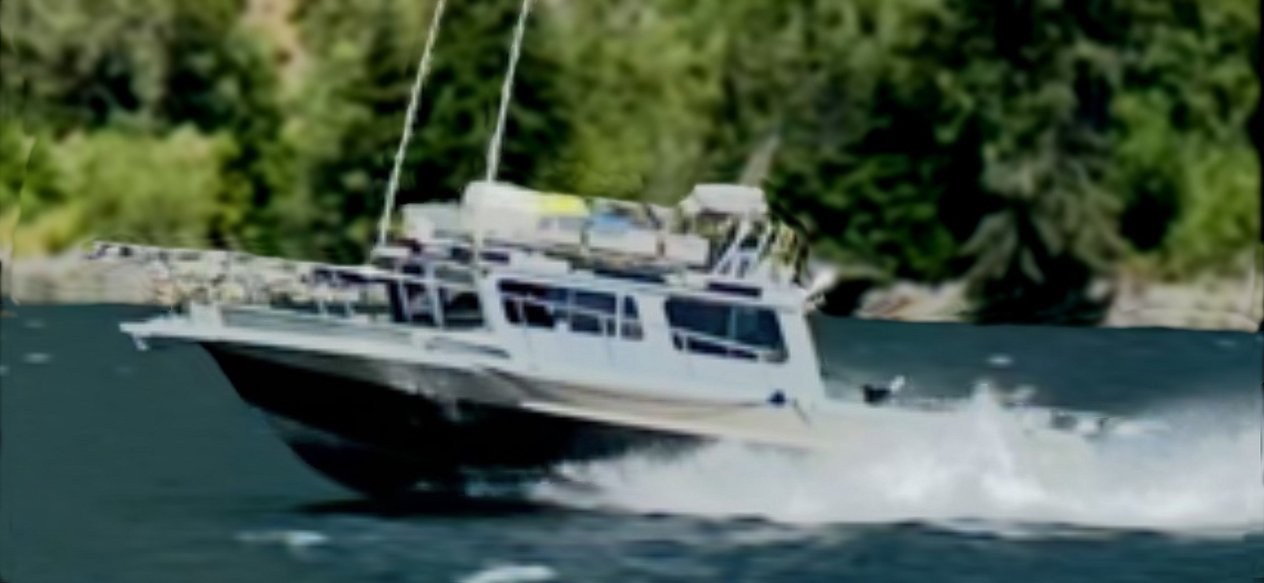 A 2014 / 3025 Kingfisher Destination Pkg speeds across a lake, creating splashes as it goes. Trees and greenery are visible in the blurred background.