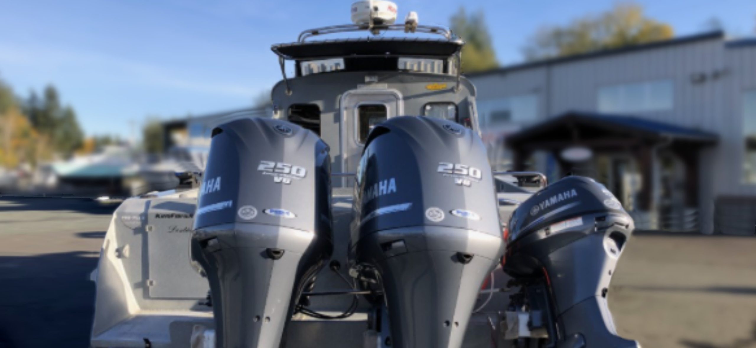 A 2014 / 3025 Kingfisher Destination boat, equipped with three Yamaha outboards including two 250 V6 engines, is parked outside a building on a sunny day.