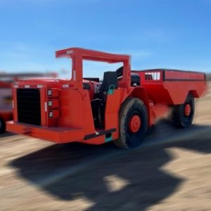 A 2014 Sandvik EJC 415 Underground Haul Truck with large black tires and an open cab is parked on dirt under a clear blue sky, showcasing its industrial heavy-duty red design.
