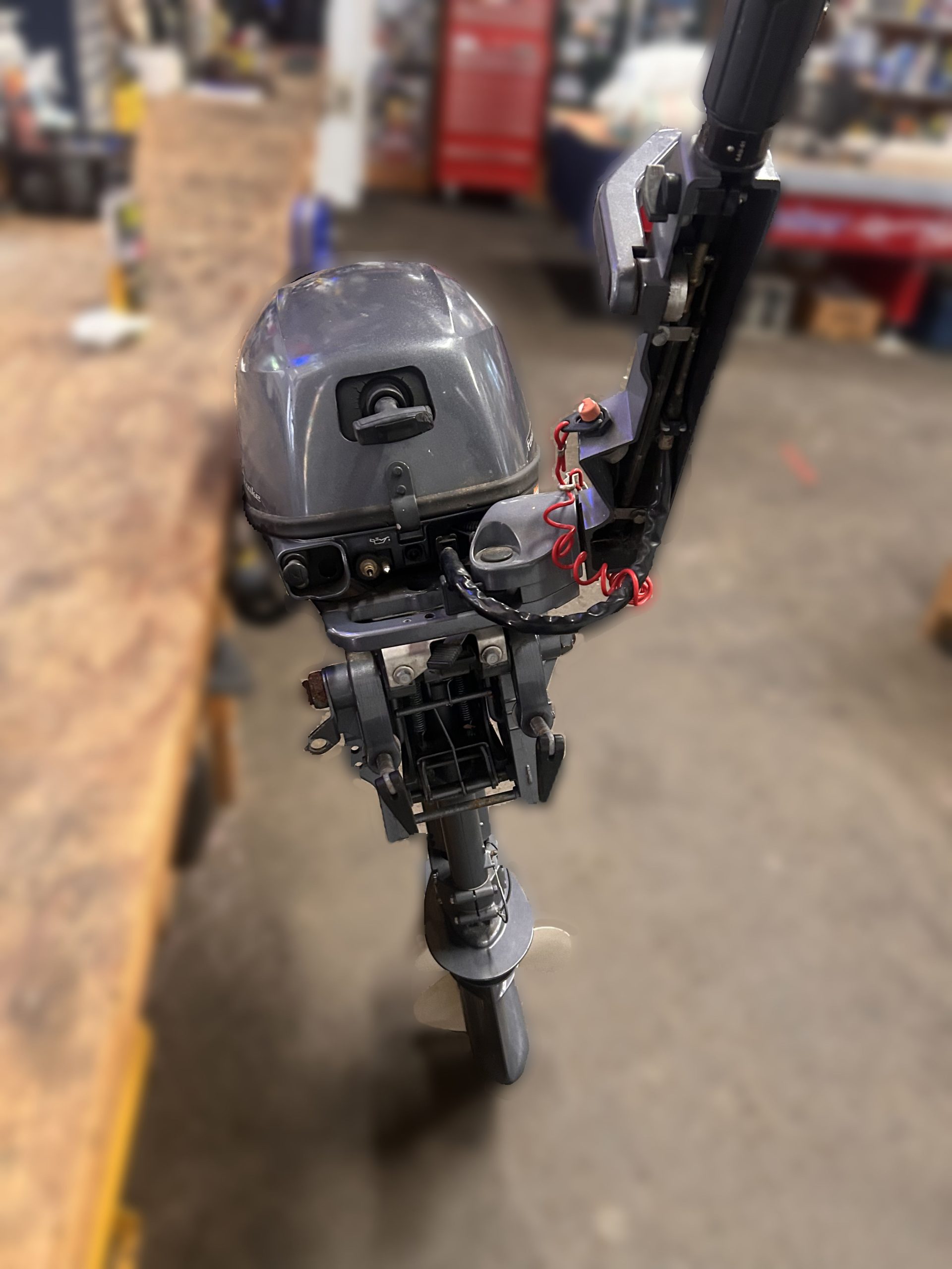 A 2014 Yamaha 9.9 HP Outboard High Thrust is mounted upright in a workshop, with tools and workbenches visible in the background.