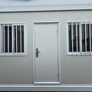 Exterior wall of a 2026 20FT Mobile Office featuring a central door flanked by two windows with vertical security bars.